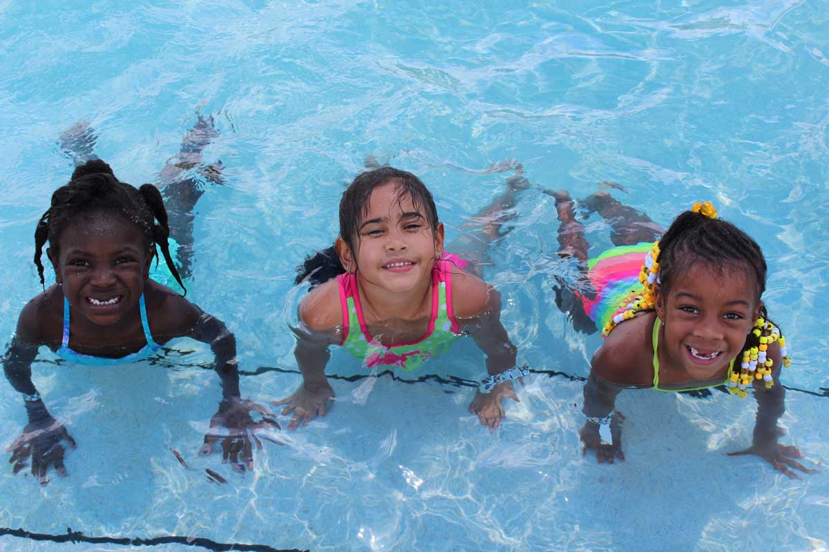 Two children swimming in a pool and smiling at the camera during a Cops 'n Kids activity