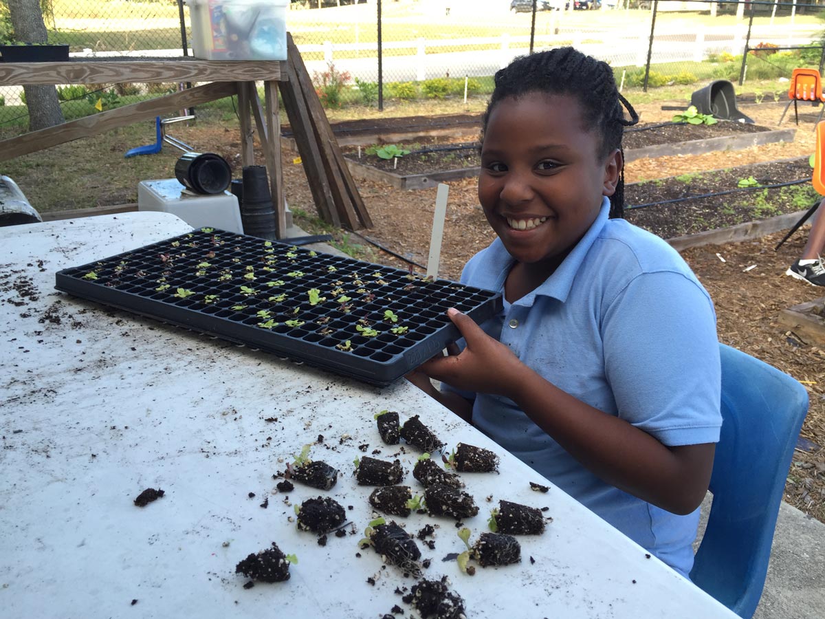 Child smiling while holding a seed starting tray in the Cops 'n Kids garden program
