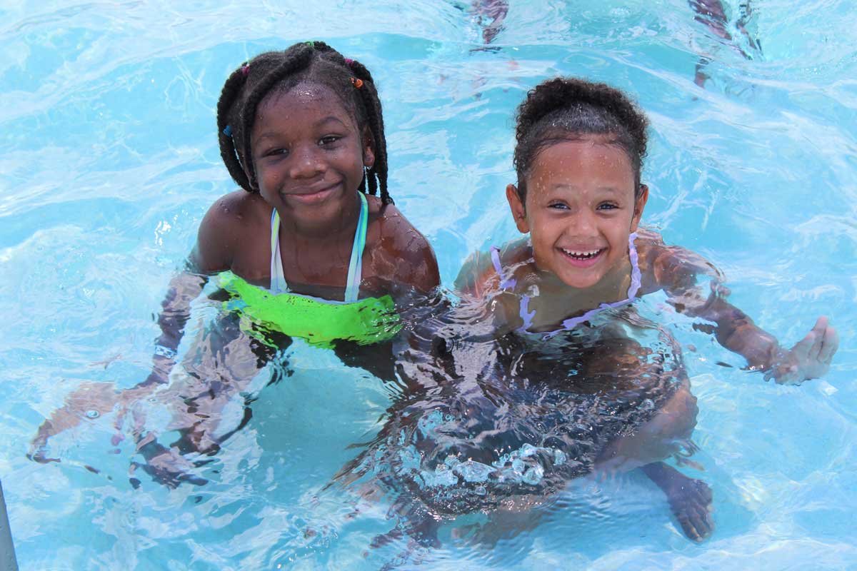 Children laughing and splashing in a swimming pool during a Cops 'n Kids summer activity